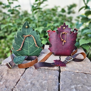 May include: Two leather leaf-shaped pouches in green and burgundy, with brown straps and buckles. The green pouch has a lighter green leaf accent on the strap. The burgundy pouch has a red interior.