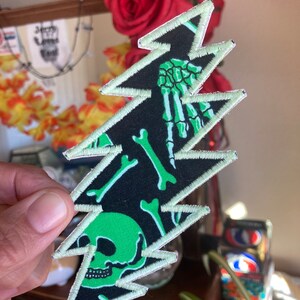 May include: Green and black embroidered patch with a lightning bolt design. The patch features a skull and crossbones pattern.