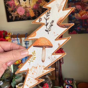 May include: A white lightning bolt-shaped patch with an embroidered brown border. The patch features a watercolor design of mushrooms, leaves, and other botanical elements in shades of orange, brown, and green.