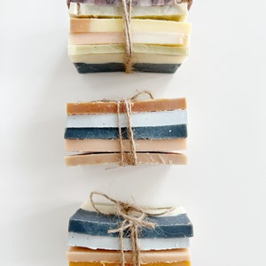 May include: A stack of handmade soap bars tied together with twine. The soap bars are in various shades of brown, beige, and grey.