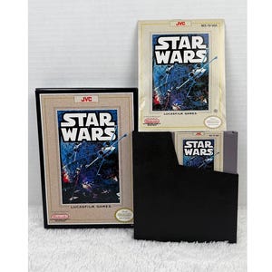 May include: A collection of vintage Star Wars video game cartridges and packaging. The game boxes feature the Star Wars logo and imagery of X-wing fighters in space. The set includes a framed box, a loose box, and a black storage case.