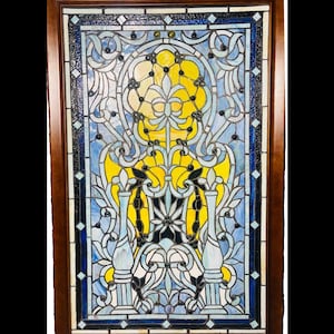 May include: A stained glass window with a brown wooden frame. The design features a central yellow floral motif, surrounded by blue and white swirling patterns. Black accents and diamond-shaped details add contrast.