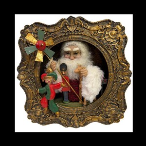 May include: A Christmas-themed decorative framed scene featuring Santa Claus, an elf, and a toy soldier. The frame is ornate with gold and brown tones. Santa holds a staff and a small deer. The elf is in red and green attire.