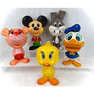 May include: A collection of five vintage cartoon character figurines. The characters include Mickey Mouse, Bugs Bunny, Donald Duck, Tweety Bird, and a pink tiger. Each figurine is brightly colored and stands on a white surface.