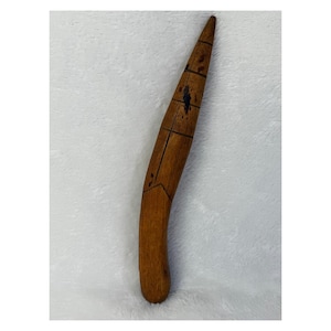 May include: A curved, wooden tool with a pointed end. The brown wood has a natural grain and is marked with dark lines and a diamond shape. The tool appears to be handmade and has a smooth, polished finish.
