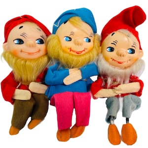 May include: Three vintage felt Christmas gnome dolls. The gnomes are wearing red, blue, and white hats and outfits. They have white beards and painted faces.