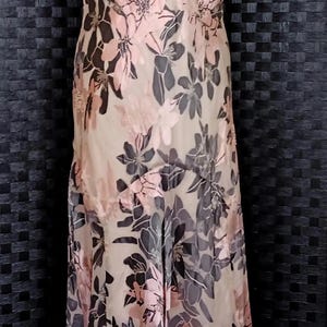 May include: A sleeveless, floor-length dress with a floral print in shades of pink and black. The dress has a cowl neck and a flowing skirt.