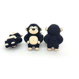 May include: Three small, black and tan monkey figurines. The monkeys have a smiling face, tan belly, and tan ears. One monkey is lying on its side, while the other two are standing upright. The text "JewelryFindings1990" is at the bottom.