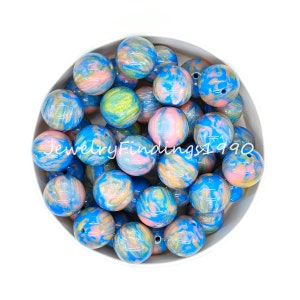 May include: A bowl filled with 20 large, round, blue, pink, and yellow marbled acrylic beads. The beads have a swirl pattern and a glossy finish.