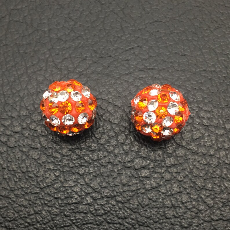 May include: A pair of orange and clear crystal stud earrings. The earrings are round and have a sparkly finish.