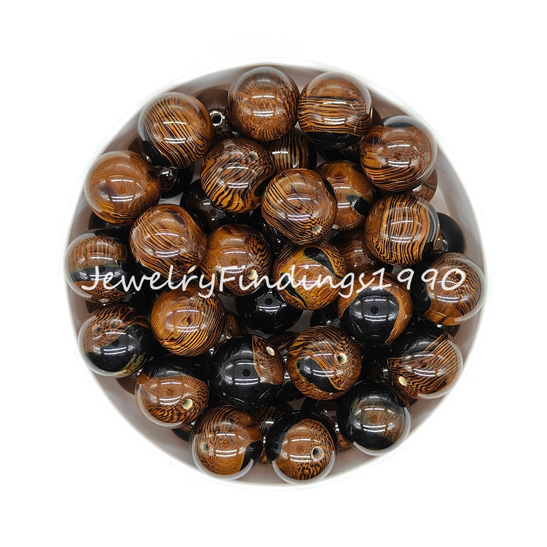 May include: A bowl of brown and black round beads with a wood grain pattern. The beads are approximately 20mm in diameter.