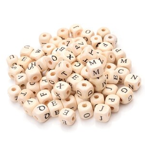 May include: A pile of natural wood letter beads. Each cube-shaped bead has a hole drilled through the center and a letter printed on each side in black. The letters are a mix of uppercase letters.