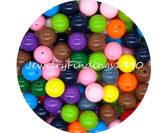 Pode incluir: Uma coleção de contas redondas de plástico coloridas em vários tons de azul, verde, rosa, amarelo, laranja, marrom e roxo. As contas têm um diâmetro aproximado de 2 cm e um acabamento brilhante.
