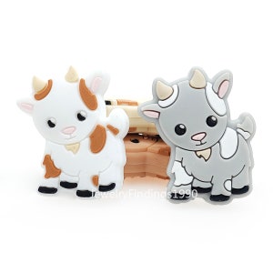 May include: Two silicone charms, one a brown and white cow and the other a grey and white goat. Both charms have black eyes and a black nose.