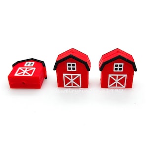 May include: Three miniature red barn figurines with black roofs and white door and window details. The barns are arranged on a white surface, showcasing their farm-themed design. The barns are a charming decorative item.
