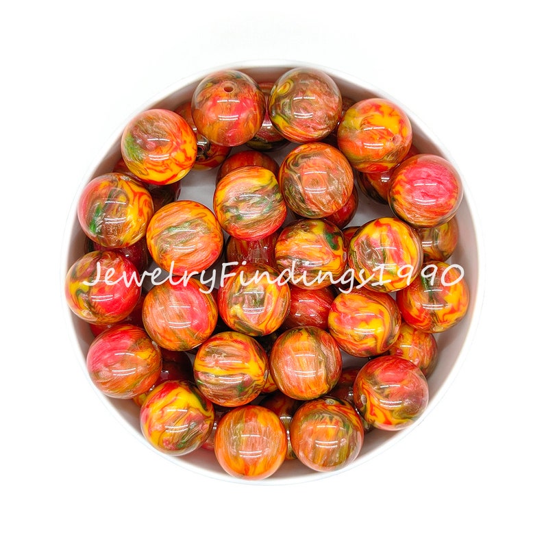 May include: A bowl filled with 20 round, colorful, swirled acrylic beads. The beads are a mix of red, orange, yellow, and green. The beads are about 2 cm in diameter.