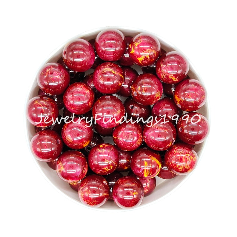 May include: A bowl of 20 red and gold marbled round beads. The beads are approximately 2 cm in diameter.