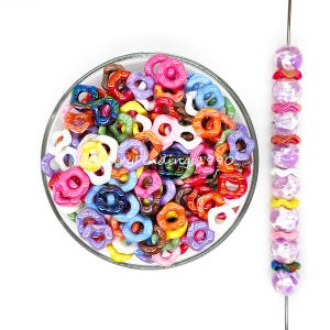 May include: A bowl filled with colourful plastic beads in various shapes, including circles, ovals, and swirls. The beads are arranged in a random pattern and are a mix of bright colours, including red, orange, yellow, green, blue, purple, and pink.