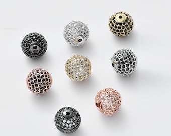 May include: Assortment of eight round, faceted beads with black, white, and gold accents. The beads are made of metal and have a sparkly finish.
