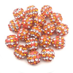May include: A group of 18 orange and clear rhinestone beads. The beads are round and have a smooth surface. They are perfect for making jewelry or other crafts.