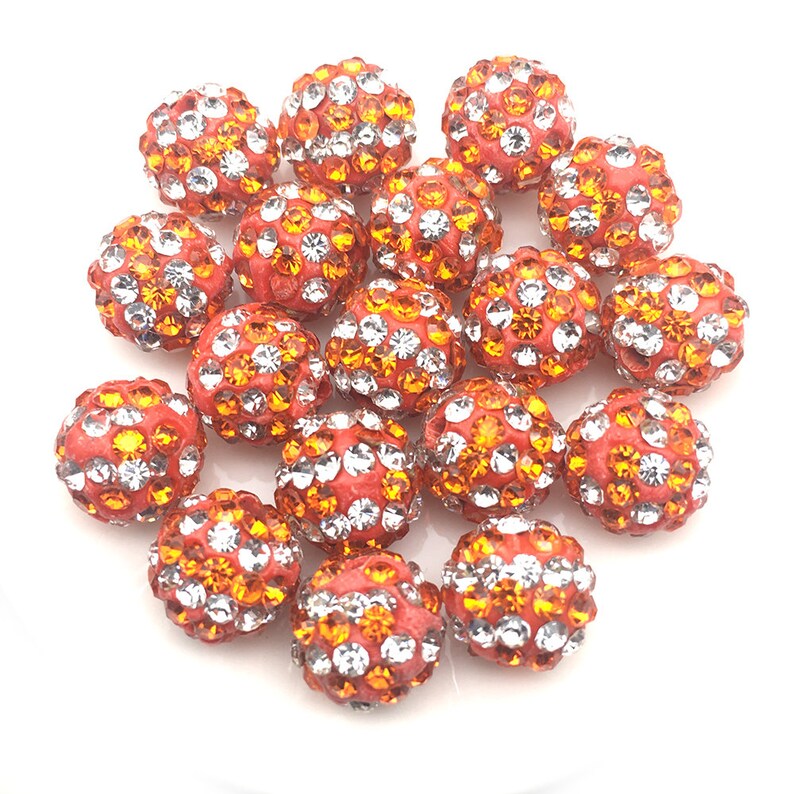 May include: A group of 18 orange and clear rhinestone beads. The beads are round and have a smooth surface. They are perfect for making jewelry or other crafts.