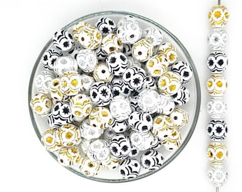 May include: A bowl filled with white, black, and gold patterned beads. The beads have a geometric design and are perfect for jewelry making or crafting.