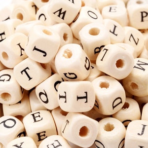 May include: A pile of natural wood letter beads. Each cube-shaped bead has a hole drilled through the center and a single black letter printed on each side. The letters are in a sans-serif font.