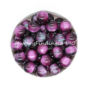 May include: A bowl of 20mm round, iridescent purple and black acrylic beads. The beads have a swirling, marbled pattern.
