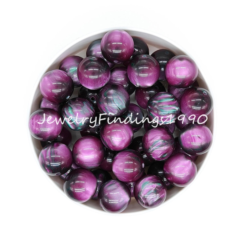 May include: A bowl of 20mm round, iridescent purple and black acrylic beads. The beads have a swirling, marbled pattern.