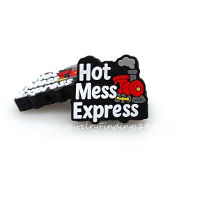 May include: Black charm with the words "Hot Mess Express" in white, featuring a red and black train illustration. The charm is designed to be attached to shoes or accessories. The charm is on a white background.