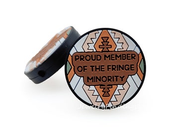 May include: Two round black silicone charms with a geometric pattern in brown, beige, and white. The charm on the right says "Proud Member of the Fringe Minority".