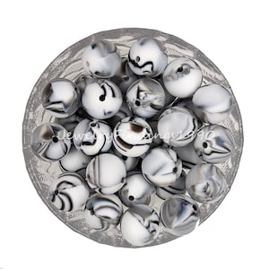 May include: A bowl of black and white marbled silicone beads. The beads are round and have a hole in the center. They are perfect for making jewelry or other crafts.