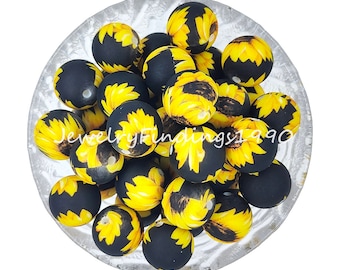 May include: A bowl filled with black and yellow silicone beads with a sunflower pattern. The beads are approximately 2 cm in diameter.