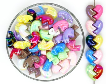 May include: A bowl filled with colorful iridescent plastic heart-shaped beads. The beads are in various shades of pink, blue, green, yellow, and purple. There is a string of similar beads in the background.