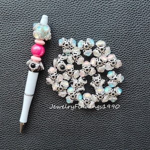 May include: A close-up of a pile of silver-toned metal bead caps with iridescent glass stones. The bead caps have a decorative design and are surrounded by clear rhinestones. The bead caps are perfect for jewelry making.