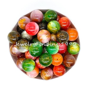 May include: A bowl filled with colorful round beads. The beads are made of a translucent material with swirls of green, orange, red, and gold. The beads are approximately 2 cm in diameter.