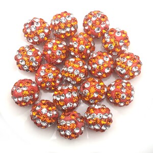 May include: A group of 18 orange and clear rhinestone beads. The beads are round and have a smooth, shiny finish. They are perfect for jewelry making or other craft projects.