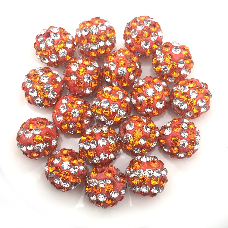 May include: A group of 18 orange and clear rhinestone beads. The beads are round and have a smooth, shiny finish. They are perfect for jewelry making or other craft projects.