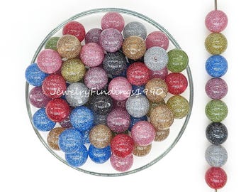 Op de afbeelding: Een kom vol met kleurrijke glitter kralen. De kralen zijn rond en hebben verschillende kleuren, waaronder roze, blauw, groen en zilver. Er is ook een kralenketting op de achtergrond.