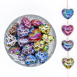 May include: A bowl of colourful heart-shaped beads with a leopard print design. The beads have an iridescent finish and are arranged in a bowl.