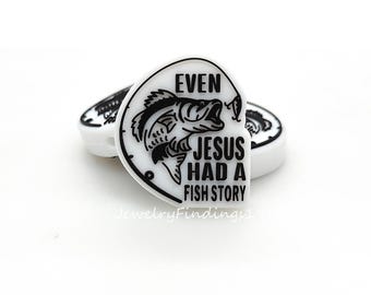 May include: White and black charm with the text "EVEN JESUS HAD A FISH STORY" and a fish graphic. The charm is in the shape of a heart. The charm is a jewelry finding.