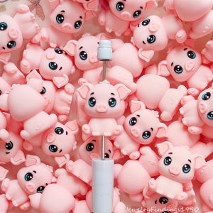 May include: A collection of small, light pink pig figurines with large blue eyes, each featuring a rounded snout and pointed ears. One pig is mounted on a thin metal rod with a white cylindrical base and a small white cap at the top of the rod.
