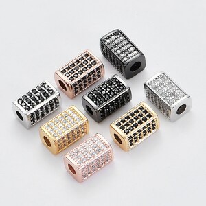 May include: Eight rectangular-shaped beads with a faceted design. The beads are in various colors, including silver, gold, black, and rose gold. Each bead is adorned with small, clear rhinestones.