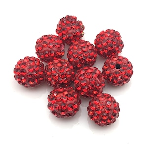 May include: A collection of ten red, round beads. Each bead is covered in small, sparkling red rhinestones. The beads are clustered together against a white background, showcasing their vibrant color and texture. These beads are ideal for jewelry making.