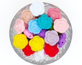 May include: A bowl filled with colourful silicone rose-shaped beads. The beads are in various colours, including pink, blue, yellow, red, purple, and white.