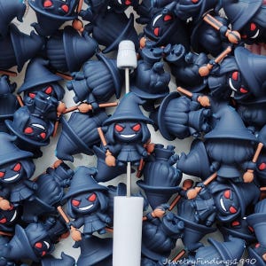 May include: A collection of dark blue witch-themed charms with red eyes and orange brooms. The charms are in various poses, some with hats and dresses. A white stylus is in the center of the image. The text "JewelryFindings1990" is in the bottom right corner.