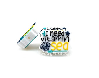 以下が含まれることがあります： 白いシリコン製のチャームで、黒い文字と青い文字で「I need vitamin sea」と書かれています。チャームには黄色の貝殻と青いヒトデが付いています。