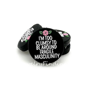 Peut inclure: Breloque noir avec une fleur rose et le texte "Je suis trop maladroite pour être autour de la masculinité fragile".