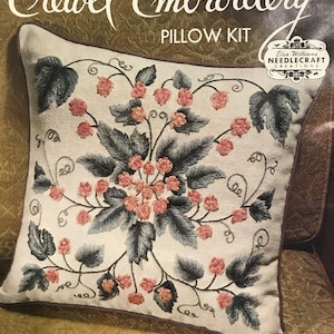 May include: An Elsa Williams Needlecraft Creations crewel embroidery pillow kit featuring a floral design with pink blossoms and dark green leaves on a light fabric. The packaging text includes dimensions of 31.75 cm by 36.83 cm.