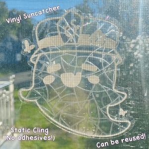 Puede incluir: Un atrapa-sol de vinilo blanco con un diseño de fantasma. El fantasma lleva un sombrero con una estrella. El atrapa-sol es de adherencia estática y se puede reutilizar. El texto "Vinyl Suncatcher" y "Static Cling (No adhesives!)" es visible en la imagen. El texto "Can be reused!" también es visible en la imagen.